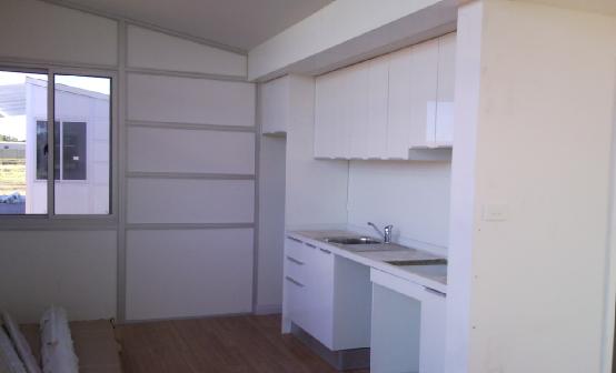 Small white kitchen inside a building with a window and cabinets.