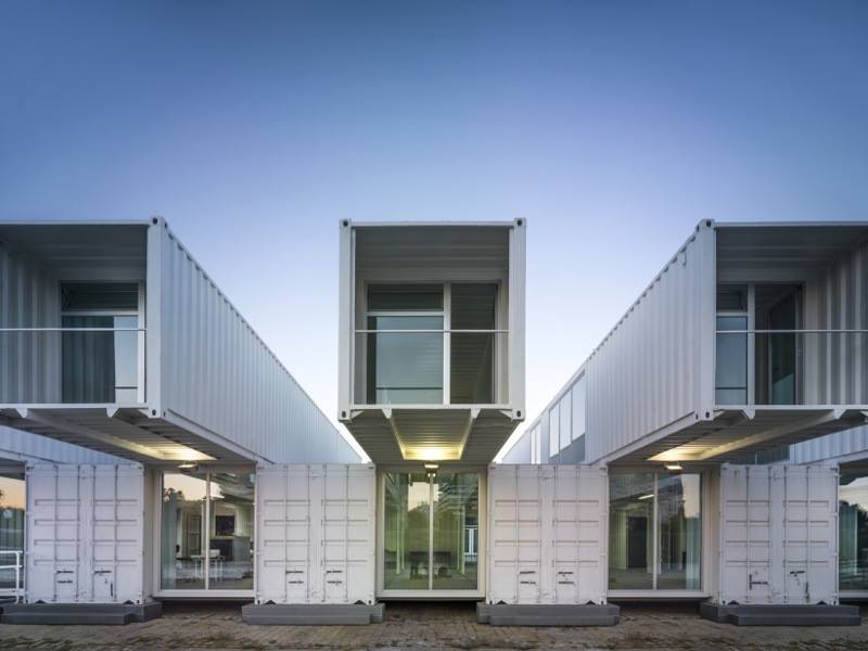 White shipping container house with glass windows and balconies against a blue sky.