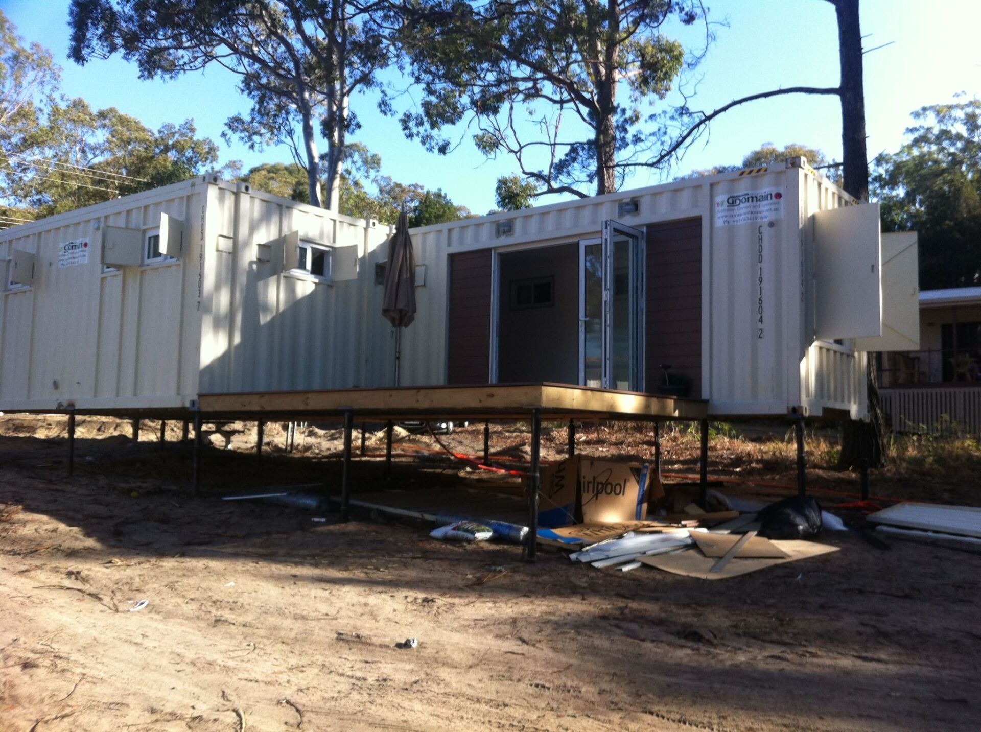 Shipping containers repurposed as a building, elevated on a wooden platform, with an open doorway.