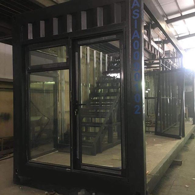 Steel-framed building under construction, featuring glass doors/windows, stairs, and structural metal supports; indoors.