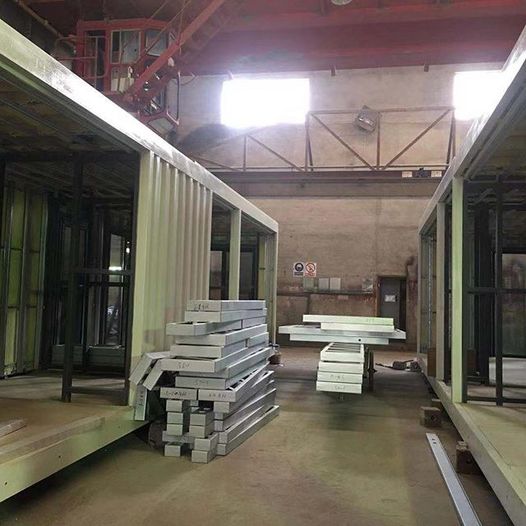 Two modular building frames in a factory, with stacked insulation and materials.