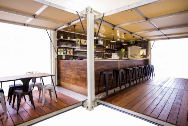 Pop-up bar with wooden bar, stools, and tables. Beige and white walls, wood floors.
