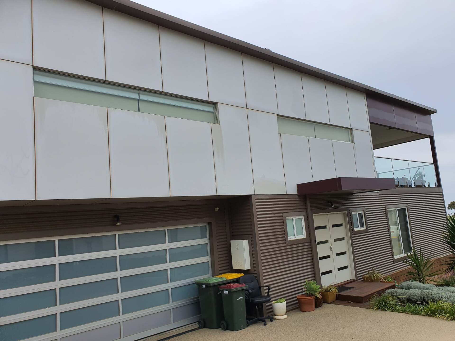 Modern house with white paneling and a glass garage door; brown wood siding and balcony.