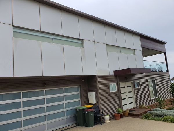 Modern two-story house with white and brown siding, a glass garage door, and a balcony. Cloudy sky.
