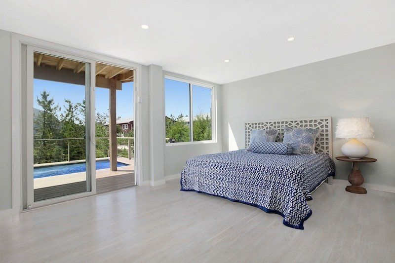 Bedroom with open sliding door to a pool and view. White walls, bed with blue and white patterned bedding.