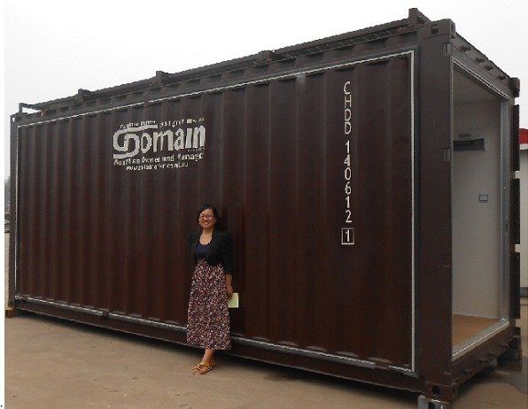 Woman stands beside a dark brown shipping container with an open doorway. 