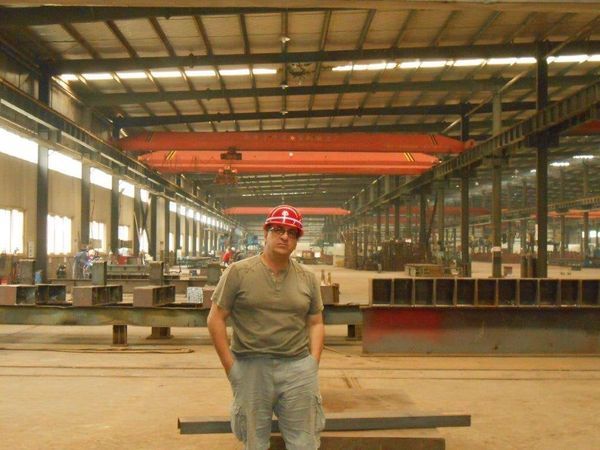 Man wearing a red hard hat, standing in a large industrial warehouse with structural steel.