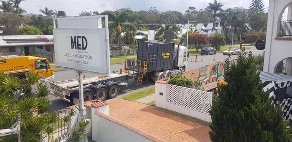 A semi-truck carrying a shipping container on a residential street. A sign for 