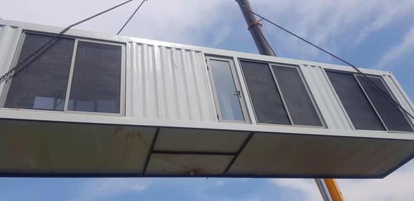 A modified shipping container, being lifted by a crane. It has windows and a door, likely a modular building.