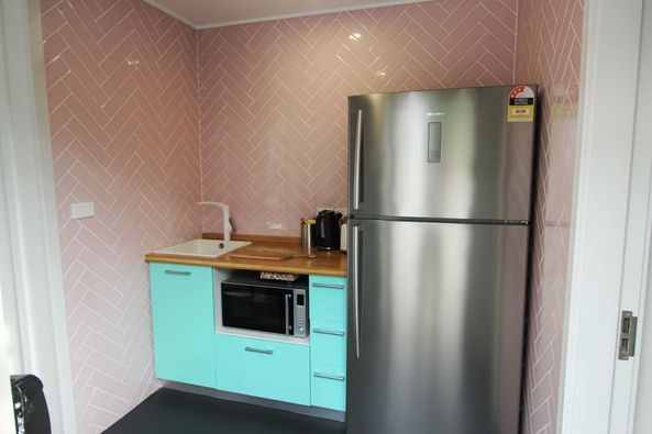 Small kitchen with teal cabinets, pink herringbone tile backsplash, and stainless steel refrigerator.