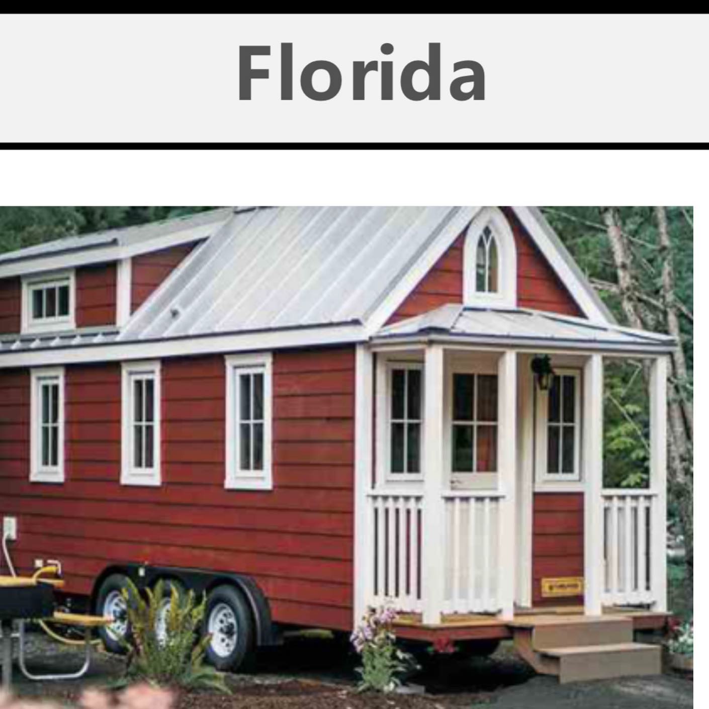 Tiny red house with white trim on a trailer, labeled 