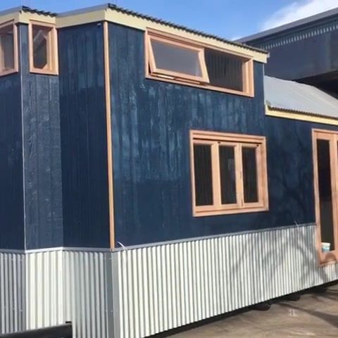 Blue and white tiny house with light-colored wooden window frames. Exterior shot, parked on a surface.