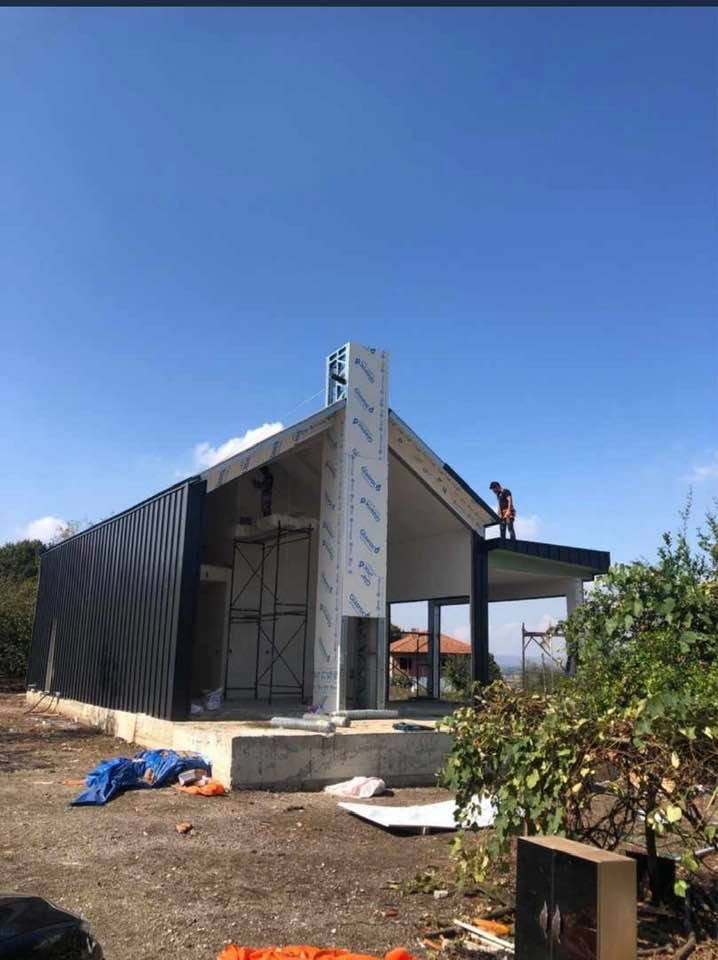 Building under construction on a sunny day; a worker on the roof. Black siding on one side of the house.