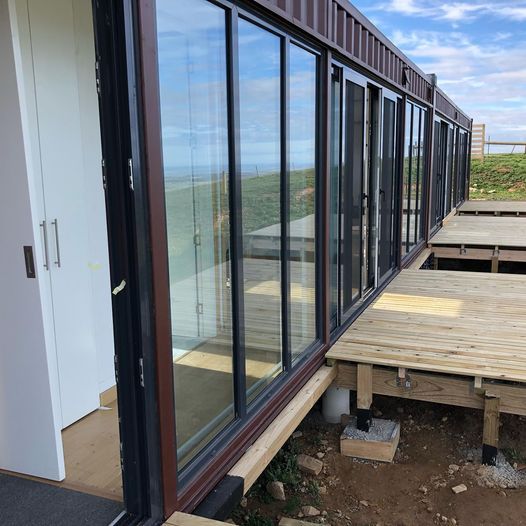 Exterior view of a modern cabin with large glass sliding doors and wooden deck.