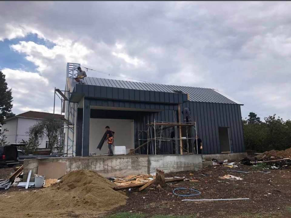 Construction workers installing metal siding on a building under cloudy skies.