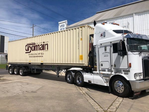 White semi-truck hauling a tan shipping container with 