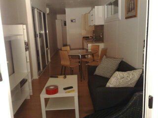 Small, narrow living space with a sofa, table, and kitchen visible.