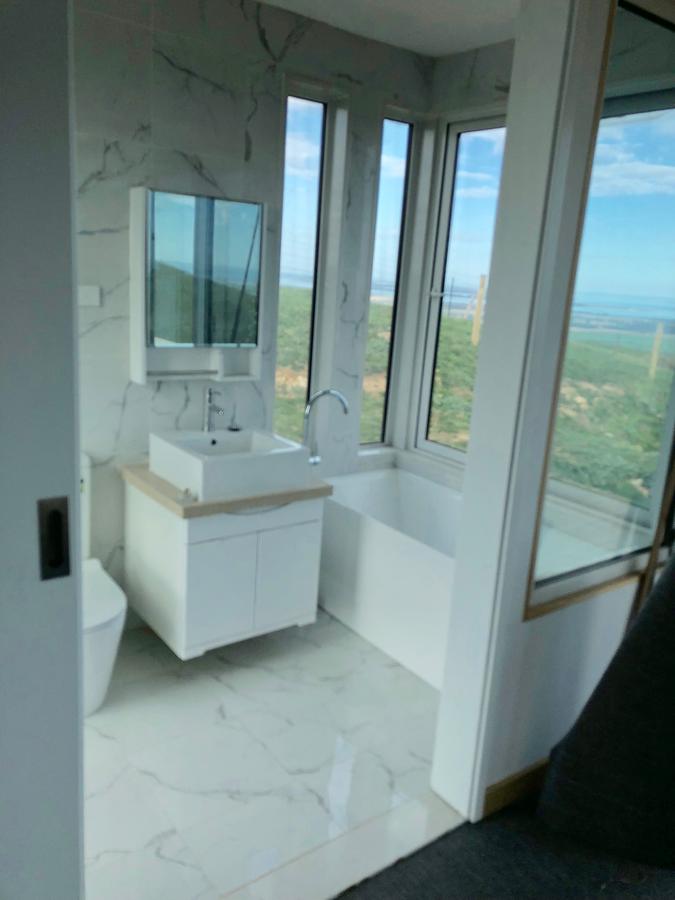 Modern white bathroom with large windows, marble tile, and a view of the landscape.
