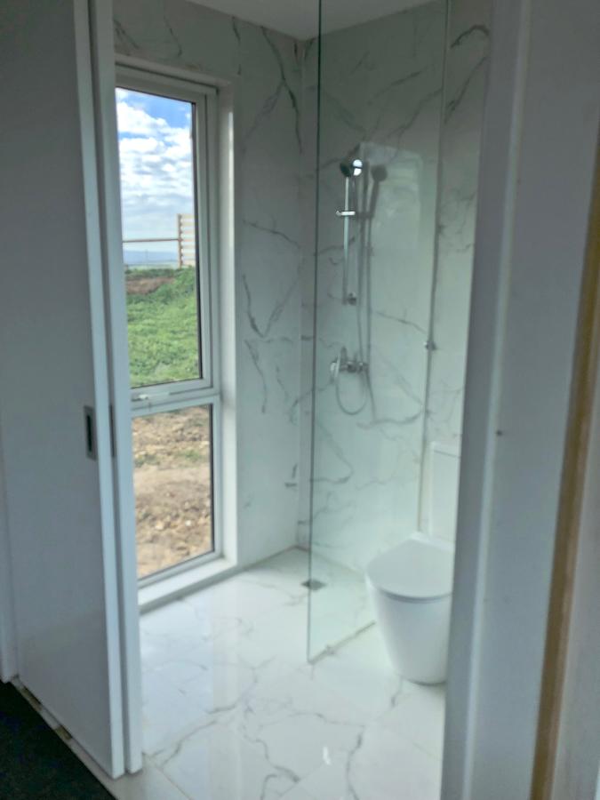 Bathroom with marble-look tile, glass shower, toilet, and window with a view of green grass and sky.