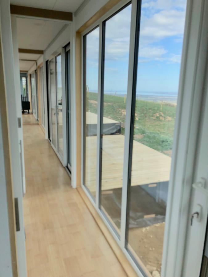 Interior hallway with large windows overlooking a beach and wooden deck.