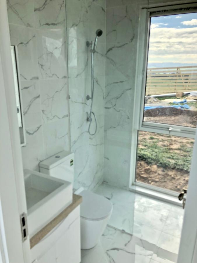 Modern bathroom with marble-look tiles, toilet, shower, and window overlooking a field and sky.