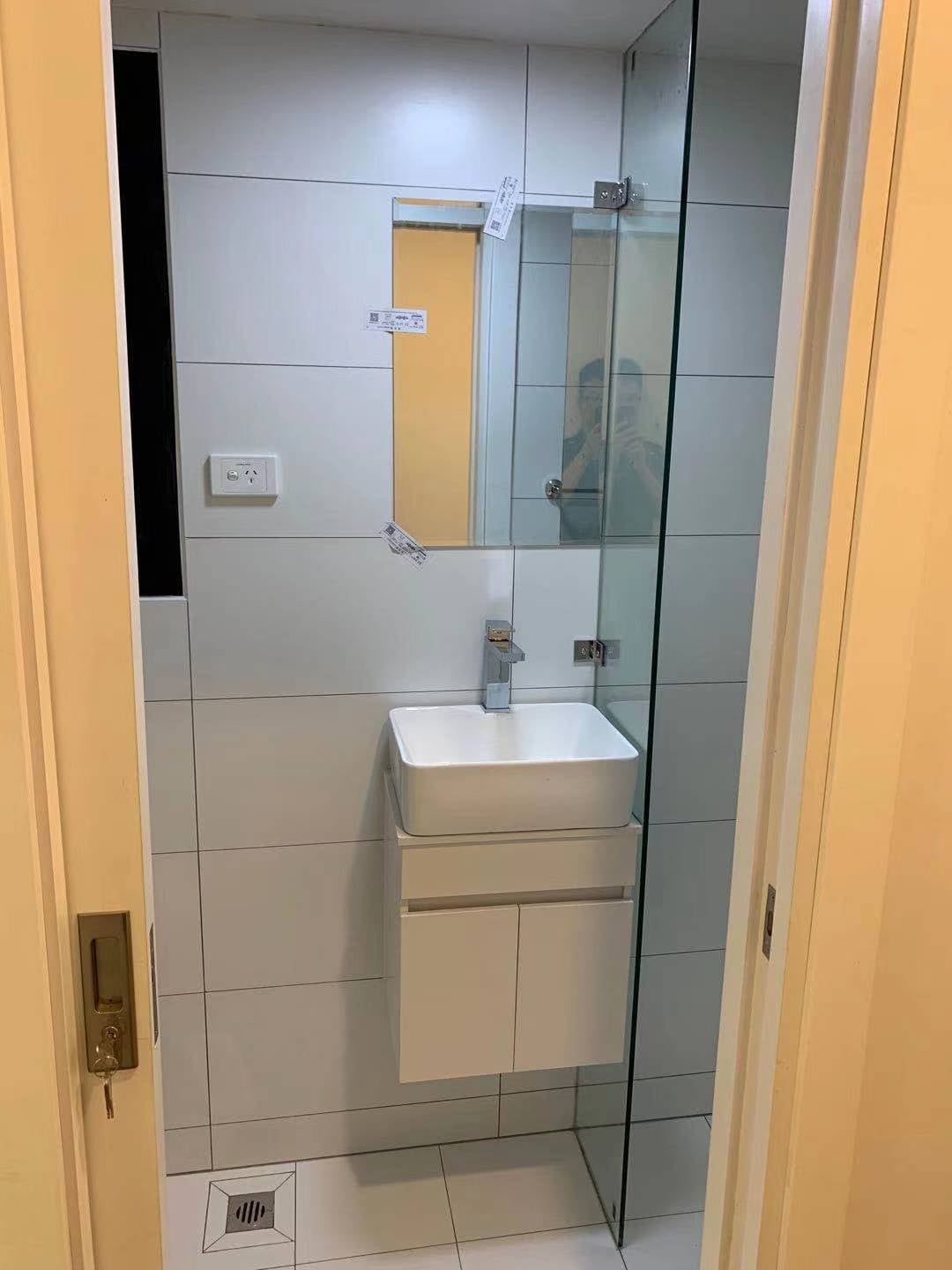 Small white tiled bathroom with a wall-mounted sink, mirror, and glass shower door.
