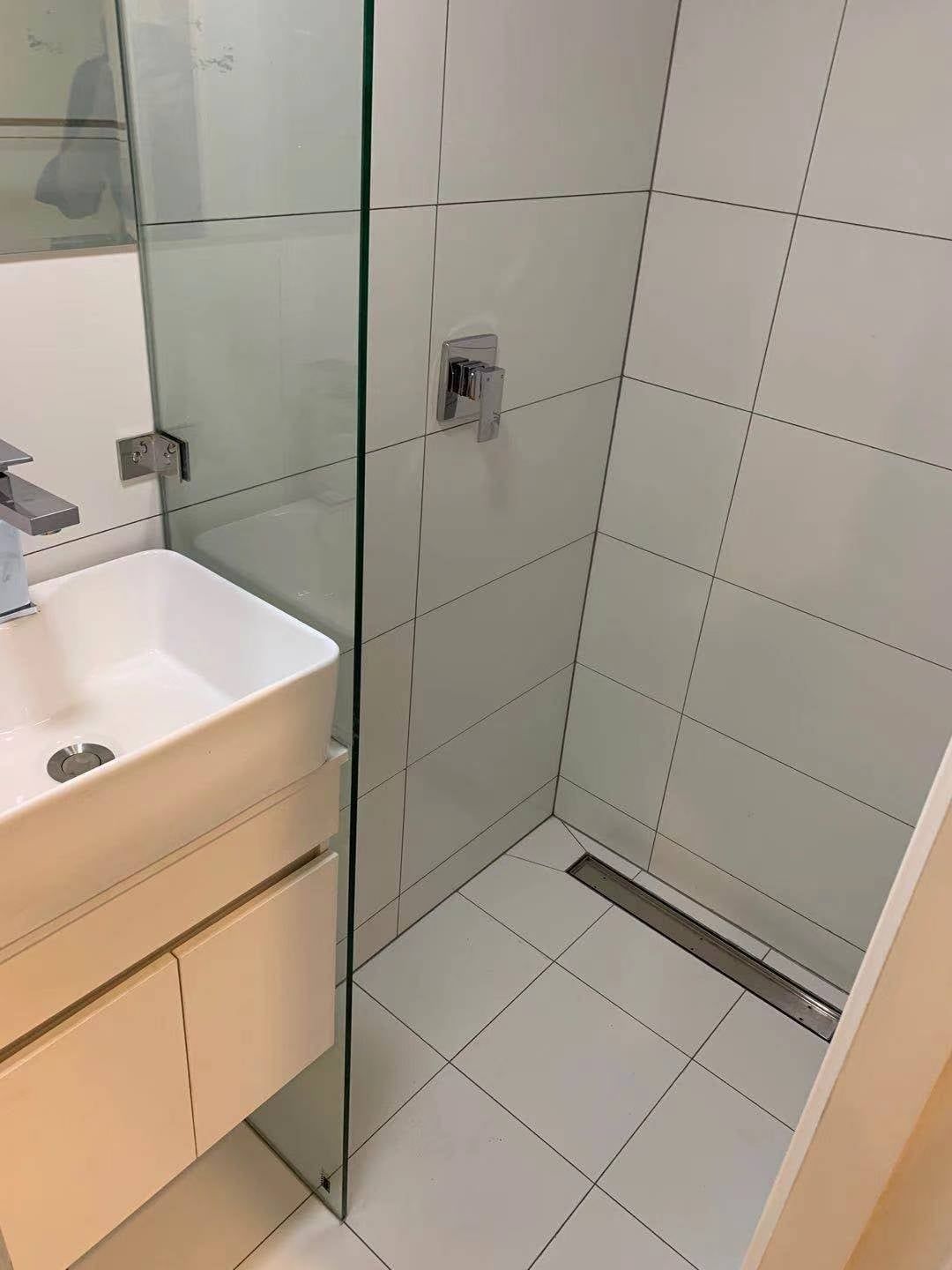 Bathroom with white tiled shower, glass door, and white sink cabinet.