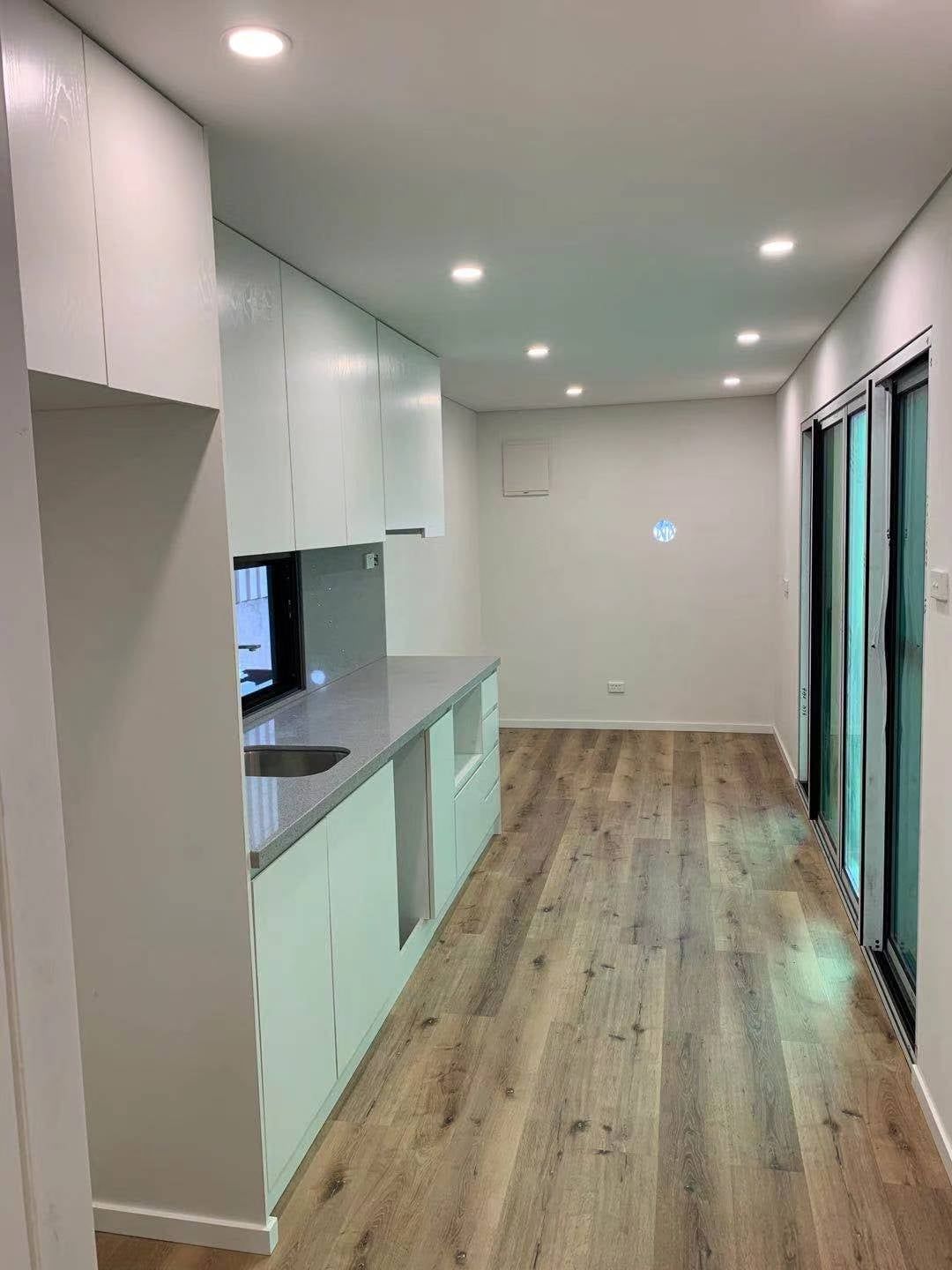 Modern kitchen with white cabinets, gray countertop, wood-look floor, and recessed lighting.