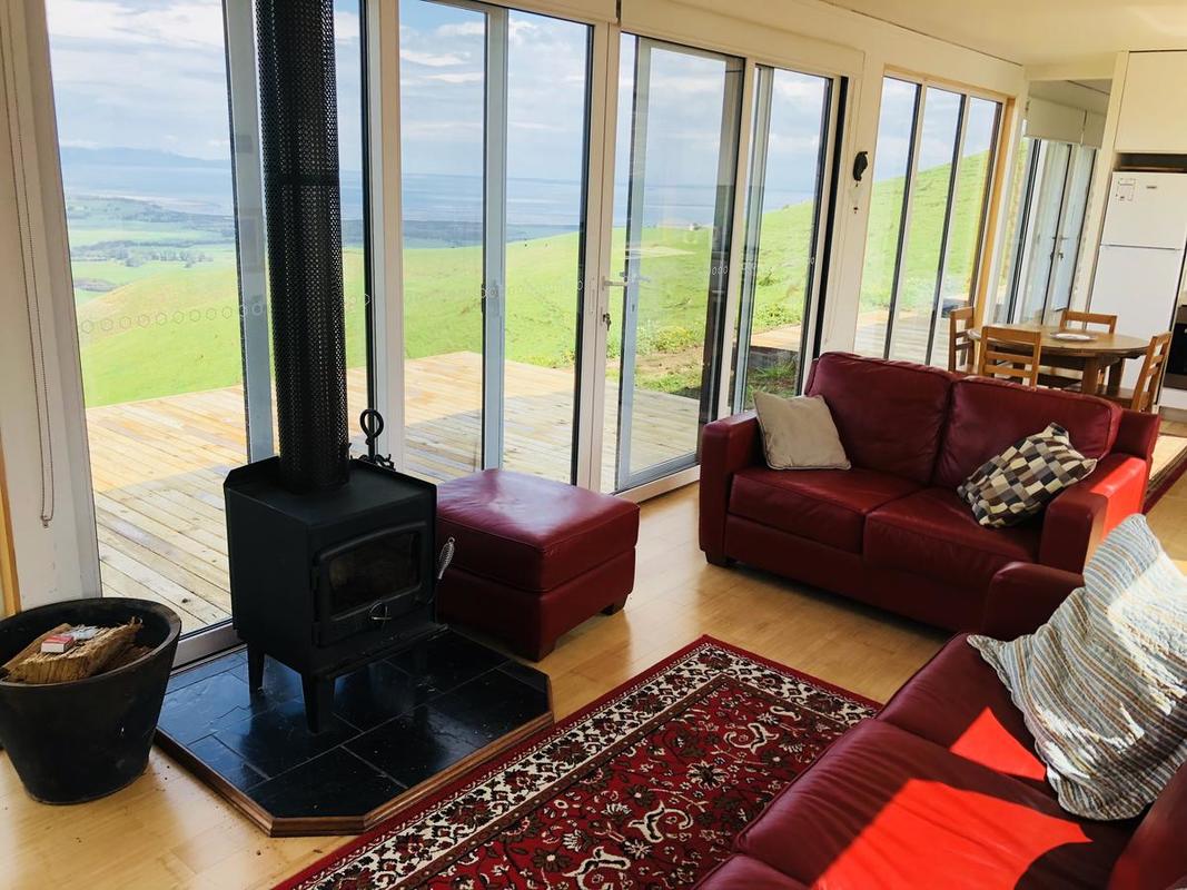 Living room with red couches, wood stove, and large windows overlooking a green landscape.