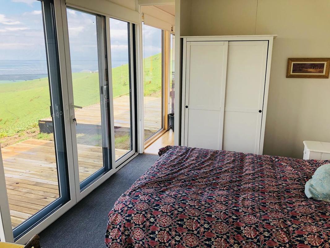 Bedroom with large windows, bed, white wardrobe, and outdoor view of green hills.