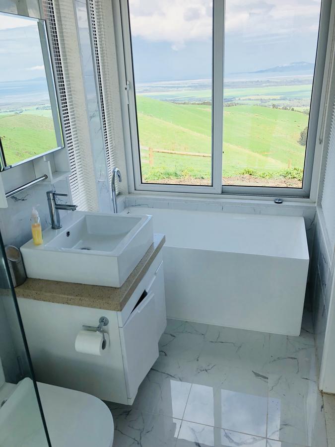 Bathroom with white fixtures, large window overlooking green landscape.