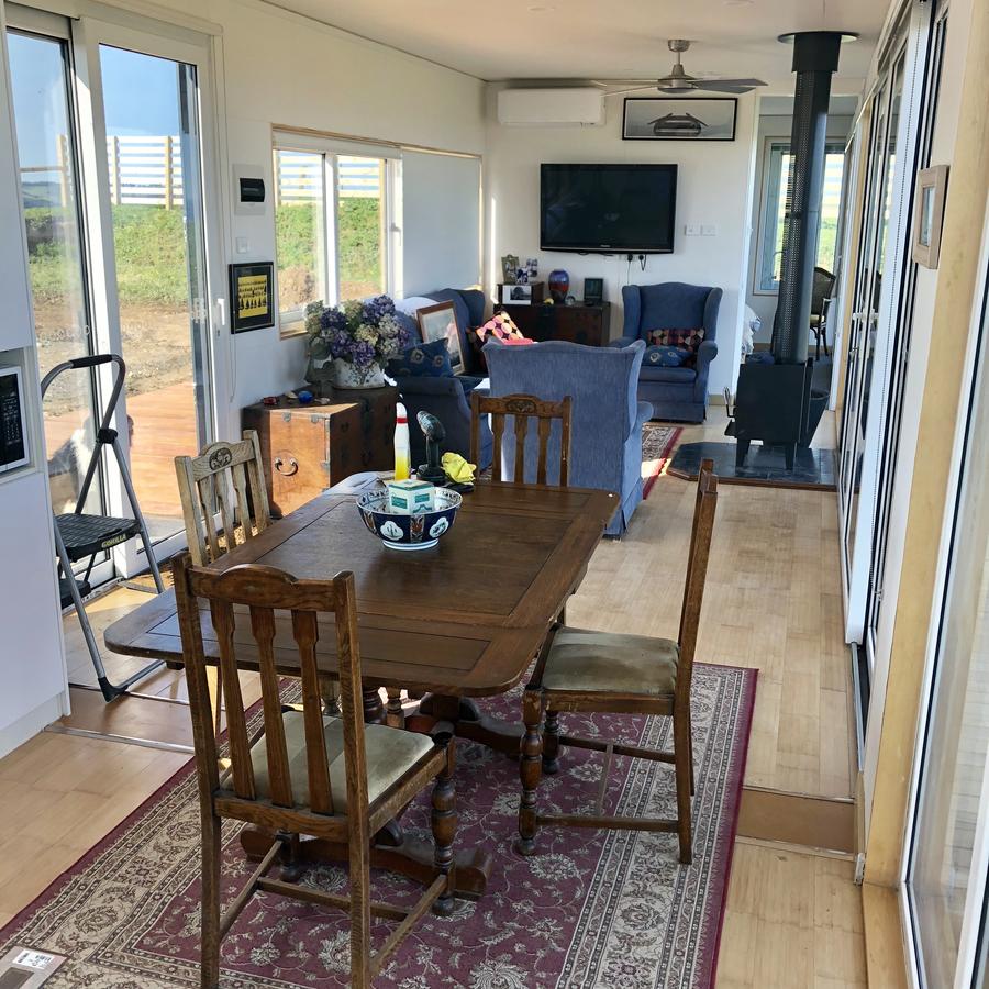 Interior view of a living/dining area with a table, chairs, sofa, fireplace, and large windows.