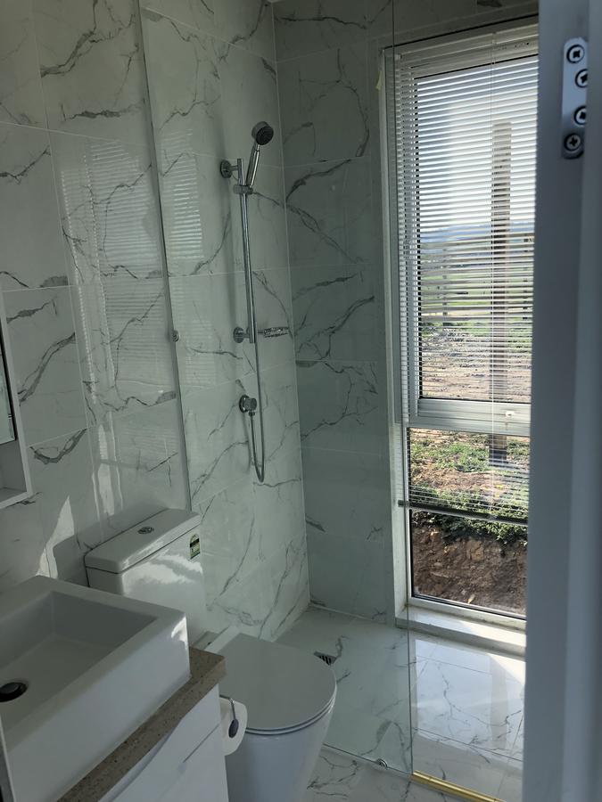 Bathroom with marble-look tile, shower, toilet, sink, and window with blinds overlooking a landscape.