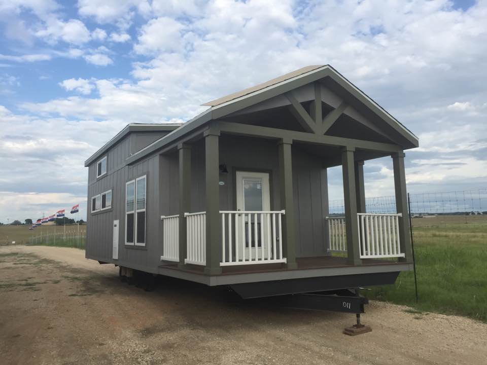 Gray tiny house on wheels with a porch, set in a field.