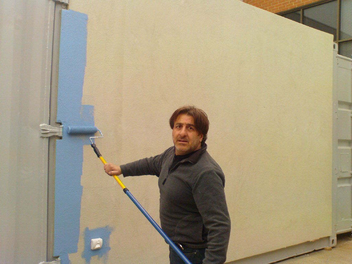 Man painting a light blue stripe on a beige wall with a paint roller outdoors.