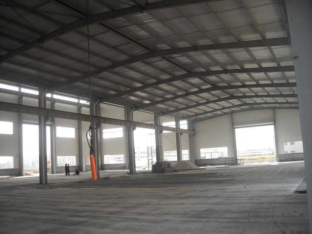 Interior of a large, empty warehouse with metal beams and pillars. Windows line the walls.