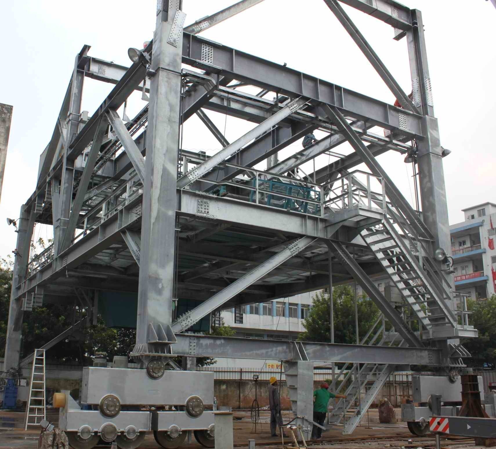 Steel framework construction, multi-level with stair access, outside, workers visible.