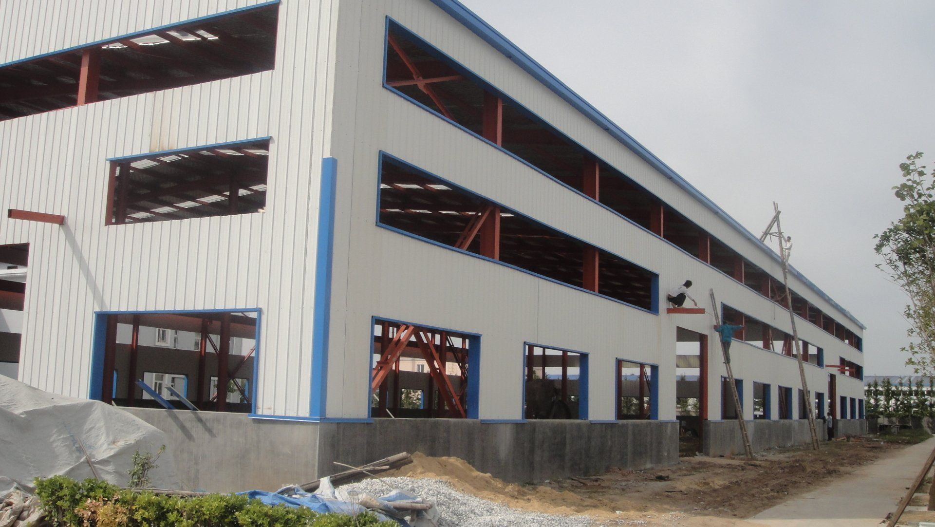 Exterior view of a large, unfinished industrial building with a white facade and exposed steel beams.