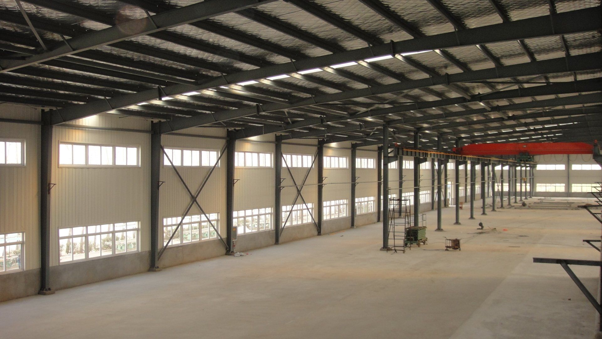 Interior view of a large, empty industrial warehouse with metal beams and walls, windows, and concrete floor.