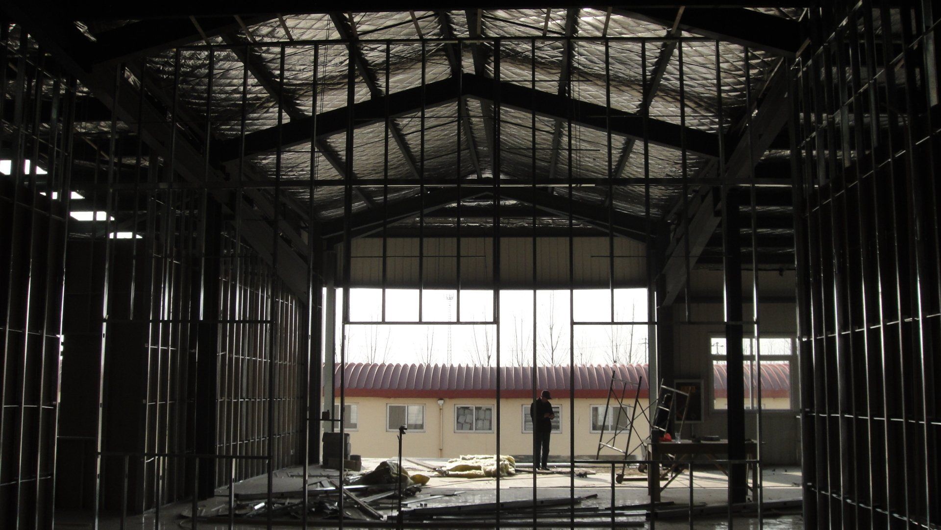 Interior view of a building under construction. A person stands in the distance framed by metal beams and a large window.