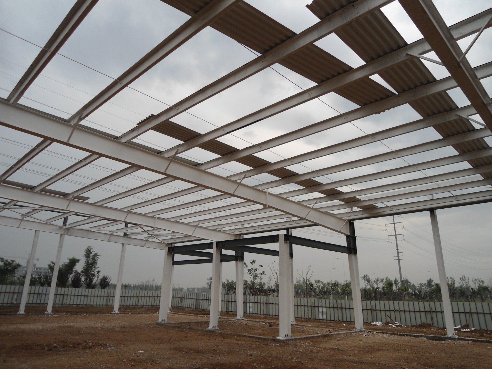 Steel framework of a building under construction, with partially installed corrugated roofing and white columns.