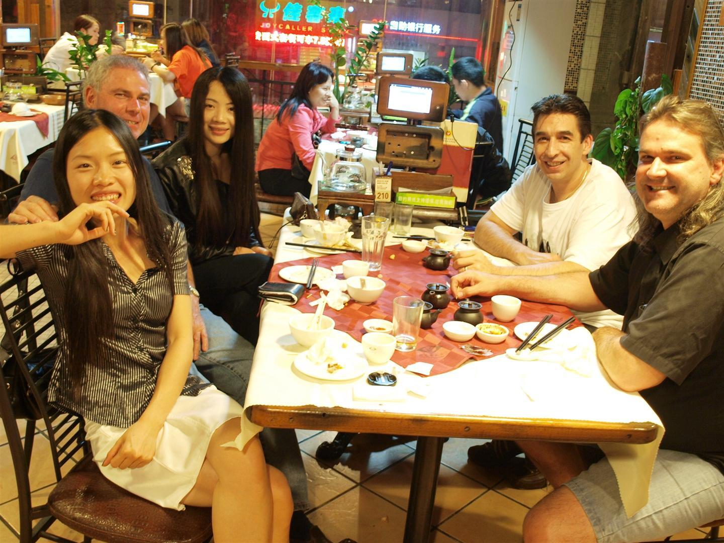 People seated at a table in a restaurant. They are smiling and interacting, with food and tea set on the table.