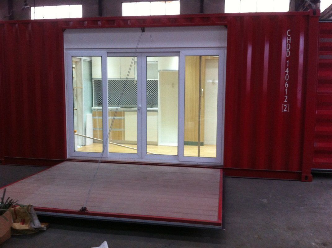 Red shipping container modified with sliding glass doors and a ramp. Inside, a well-lit space is visible.