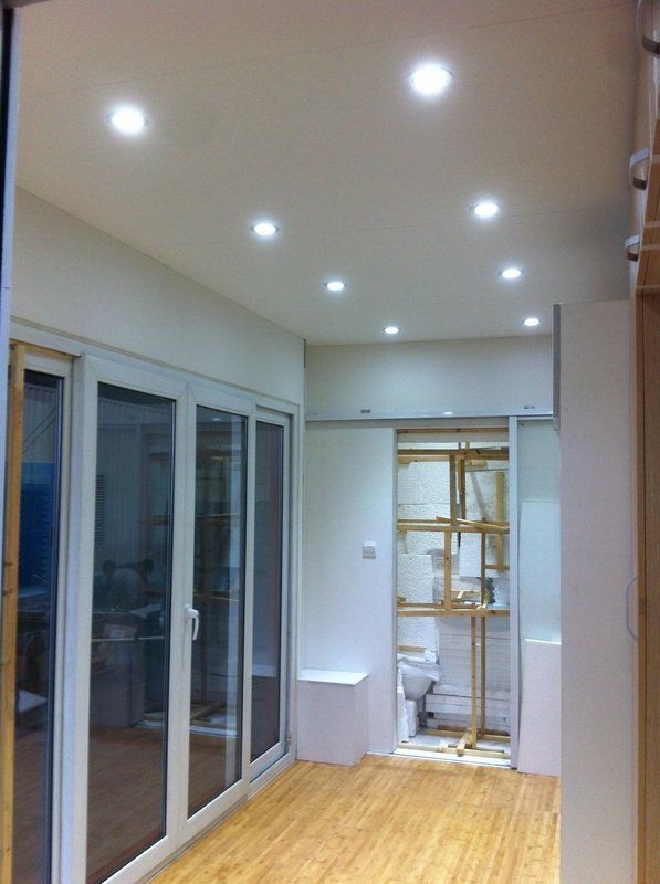 Interior of a room with recessed ceiling lights, glass doors, light wood flooring, and a partially open doorway.