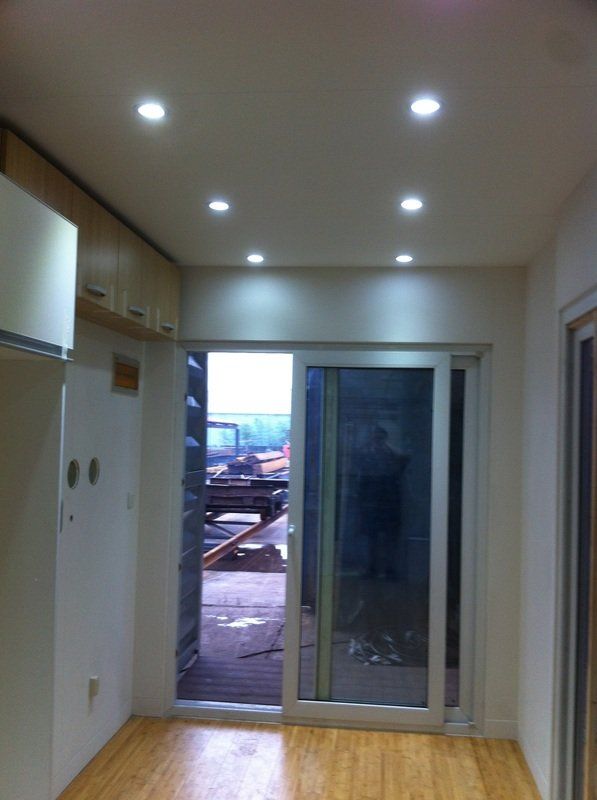 Interior of a room with recessed lighting, sliding glass door, wooden floors, and cabinets.