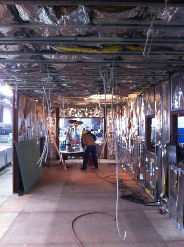 Interior construction with exposed framing, insulation, and a worker cutting a material.