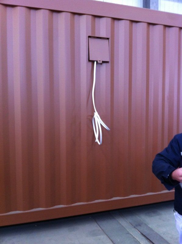 Brown corrugated metal shipping container with a white cord dangling from a square box.