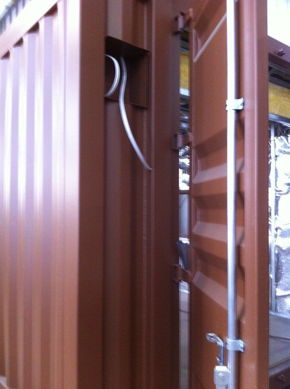 Brown shipping container with open door; metal cables enter through a side opening.
