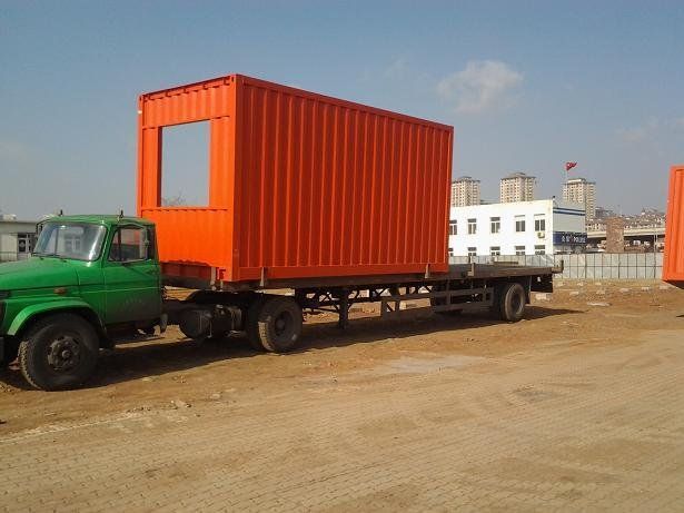 Green truck hauling an orange container with a window cut out on a flatbed trailer.