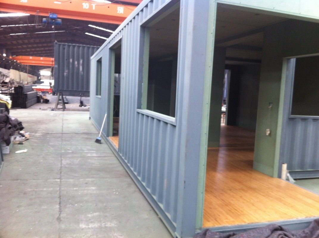 A modified shipping container painted gray with wooden floor and large windows, indoors.